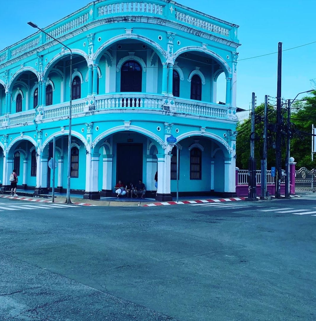 A turquoise Sino-Portuguese corner building in Phuket Old Town, shutters and arcades on a quiet crossing