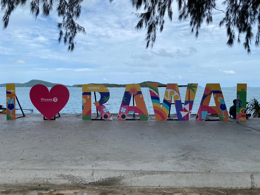The I HEART RAWAI sign on a concrete promenade, with flat water and low islands behind it — no surf and no swimming beach