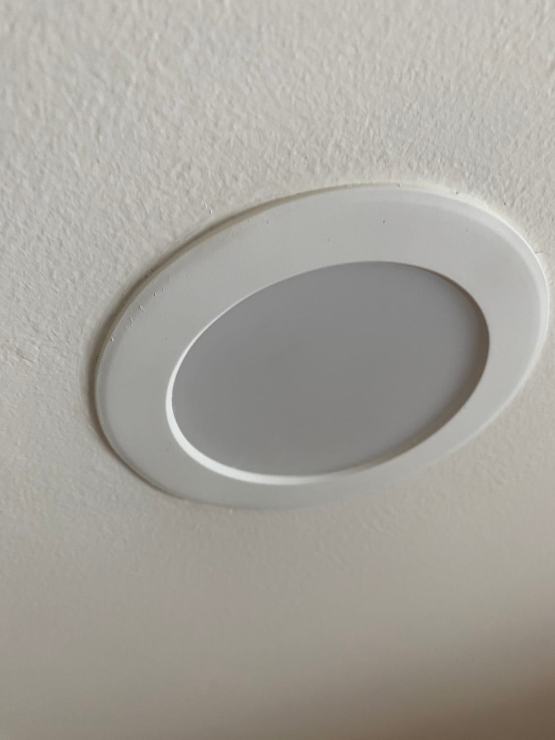 A white recessed LED downlight sitting flush in a white textured condo ceiling