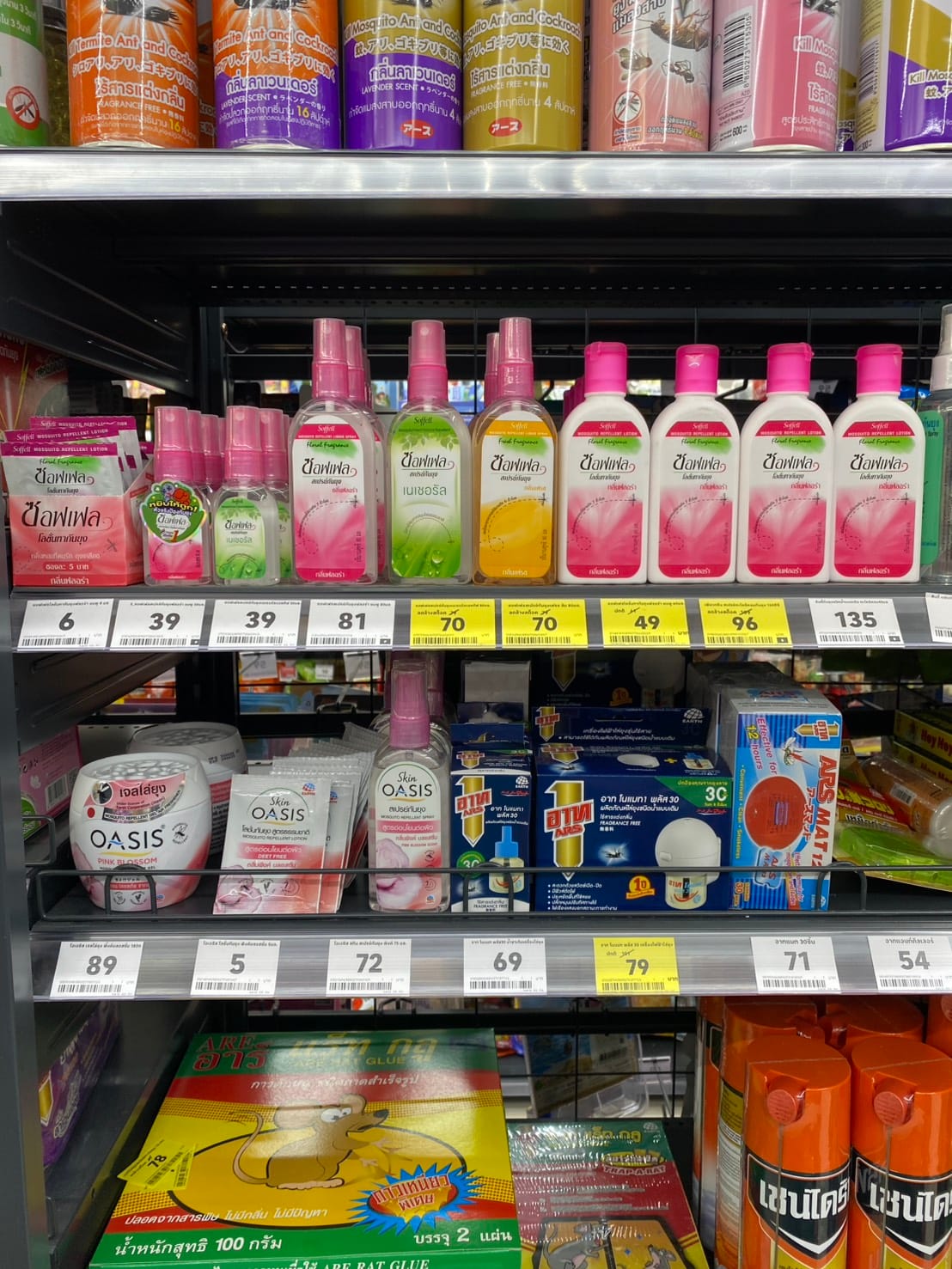A supermarket shelf of mosquito repellent in Thailand — rows of Soffell lotion bottles and pump sprays with yellow and white price tags below them reading 39, 49, 70, 81, 96 and 135 baht, and mosquito coils and plug-in mats on the shelf beneath
