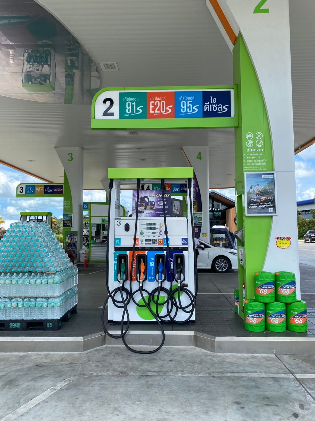 A fuel pump island at a Thai petrol station, the overhead sign reading Gasohol 91, E20, Gasohol 95 and Hi Diesel in Thai, with four colour-coded nozzles below it — green, orange, blue and black